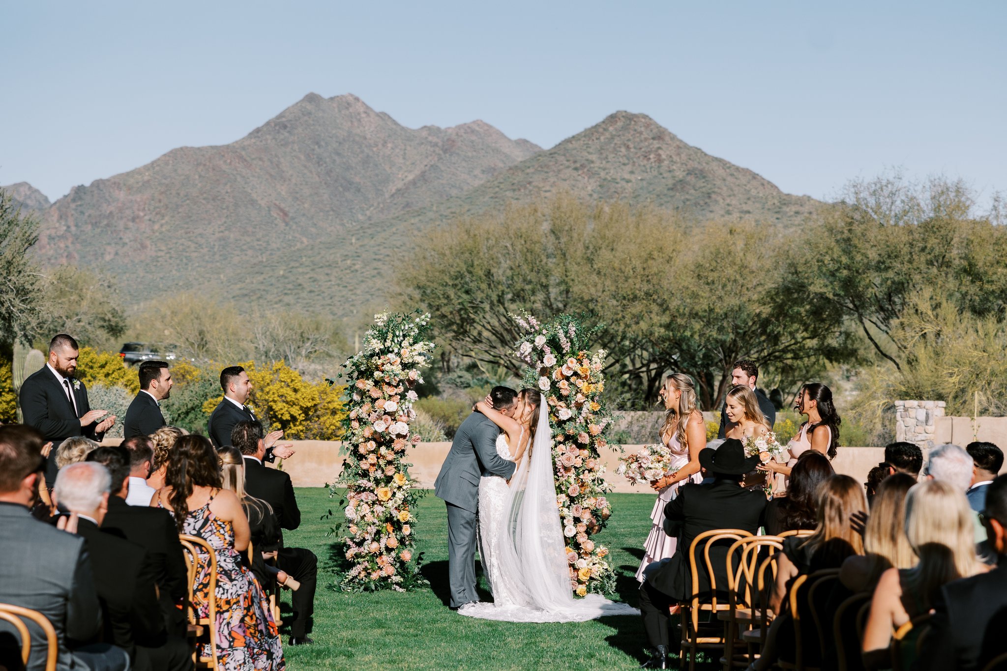 Bride and groom kissing at outdoor Windgate Ranch wedding ceremony between floral pillars.