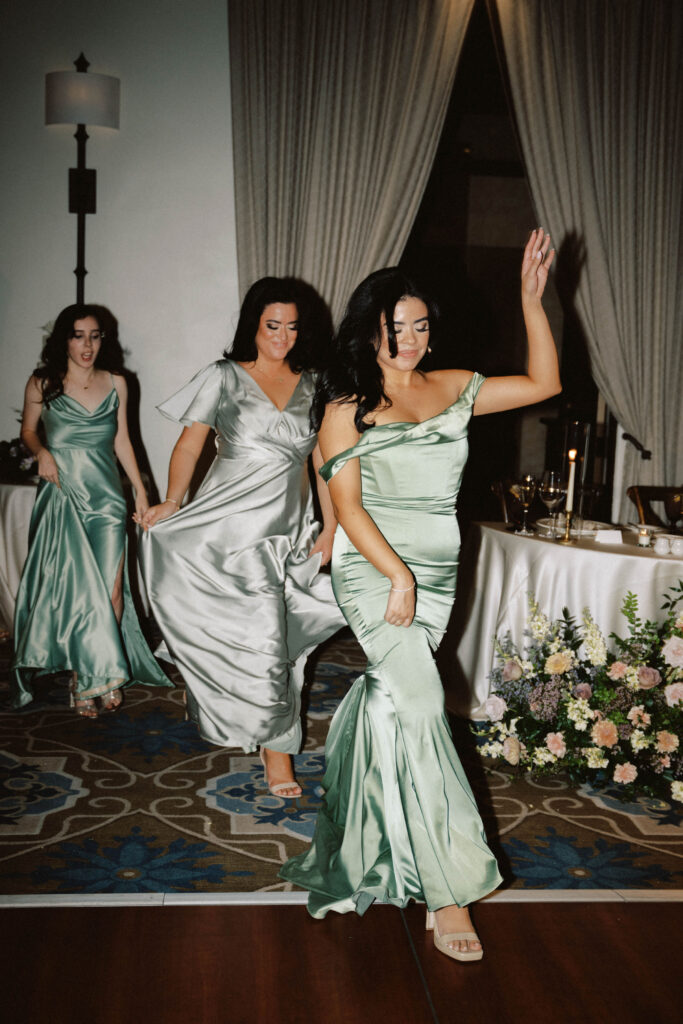 Bridesmaids entering wedding reception, holding dresses up slightly to walk.