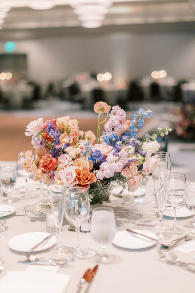 Reception table floral centerpiece of pink, peach, blue, and white flowers.