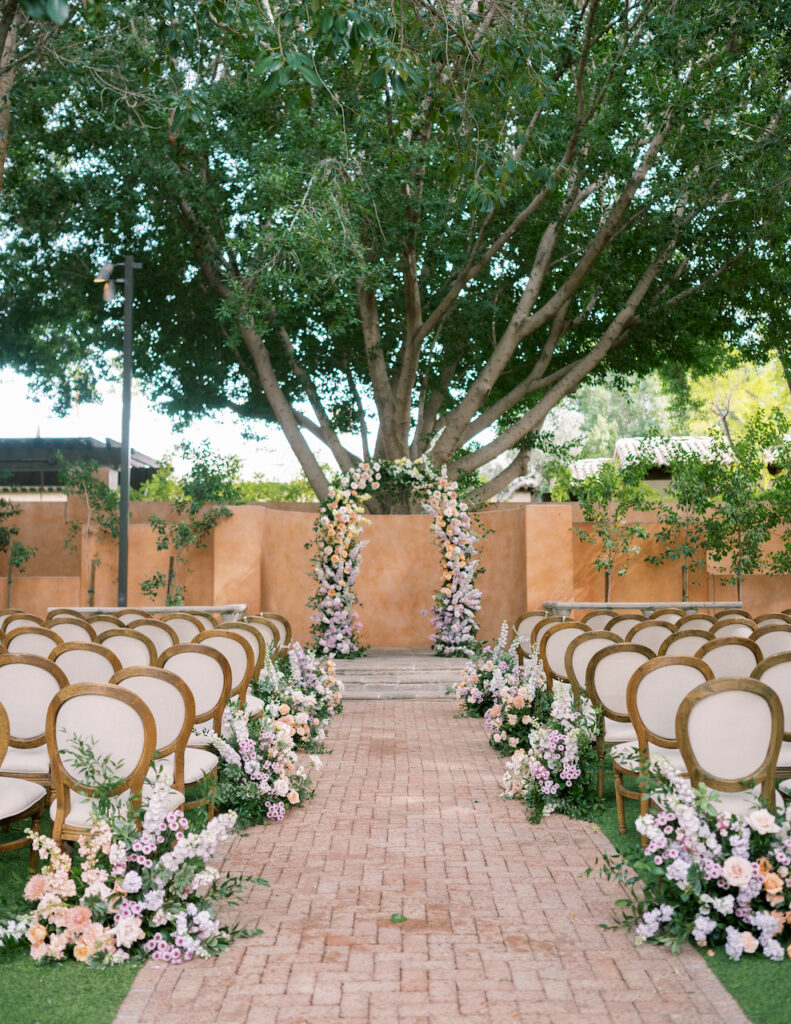 Outdoor ceremony space at Royal Palms with floral arrangements along aisle ground and floral arch in altar space.