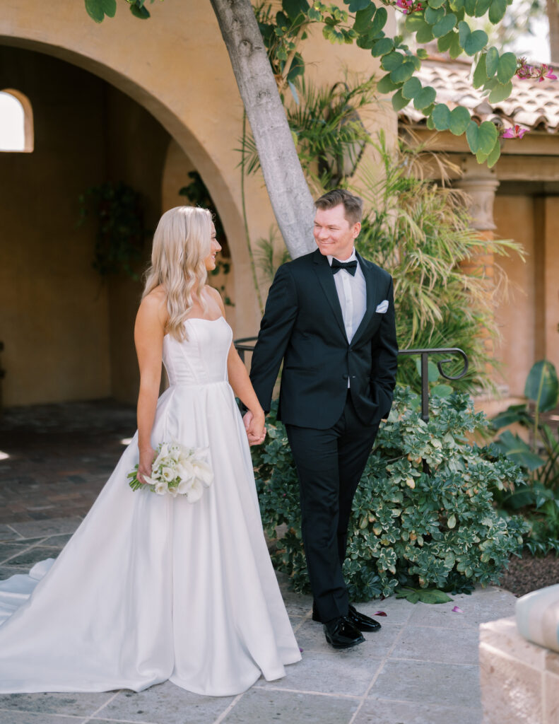 Bride and groom holding hands, smiling at each other, walking through Royal Palms outdoor path.