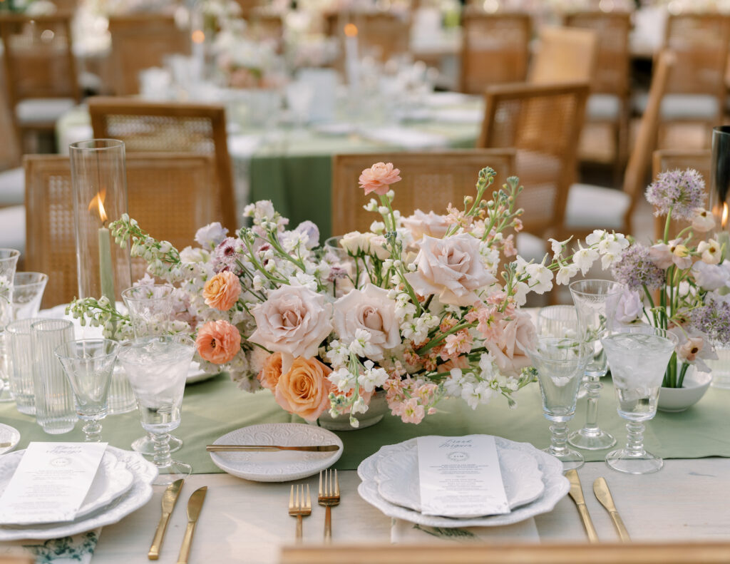 Lush floral reception centerpiece in pink, peach, and white floral shades on sage green runner down center.