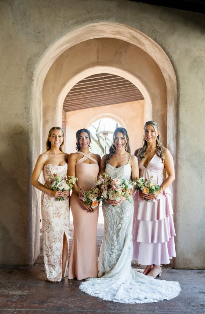 Bride with bridesmaids in pink colored dresses standing in line in archway.