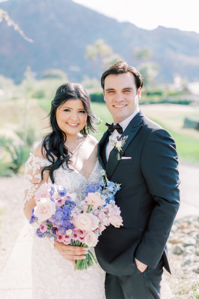 Bride and groom outside standing close, smiling, bride holding bouquet.