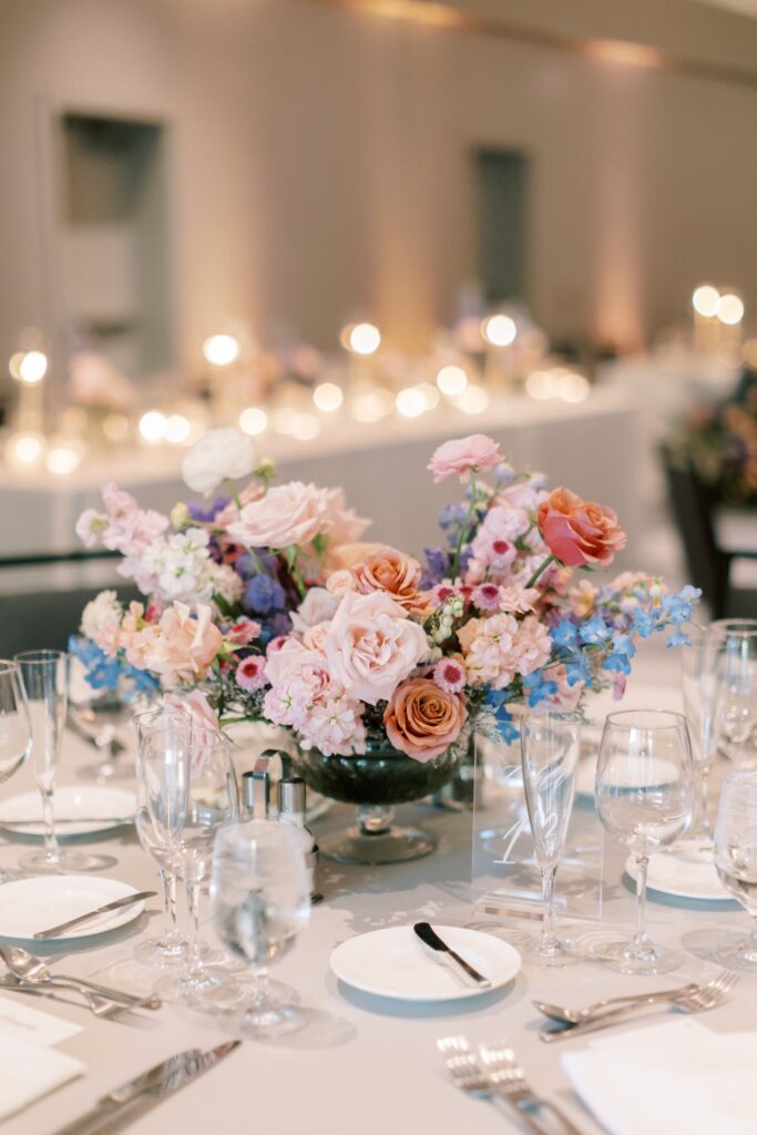 Reception table floral centerpiece of pink, peach, blue, and white flowers.