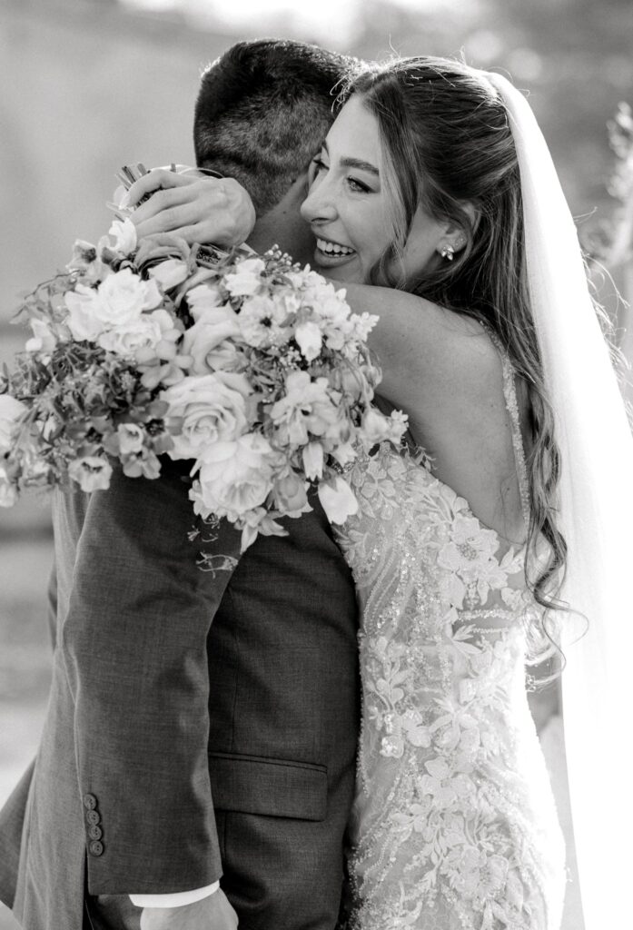 Bride with arms around groom's neck, smiling and holding bouquet.