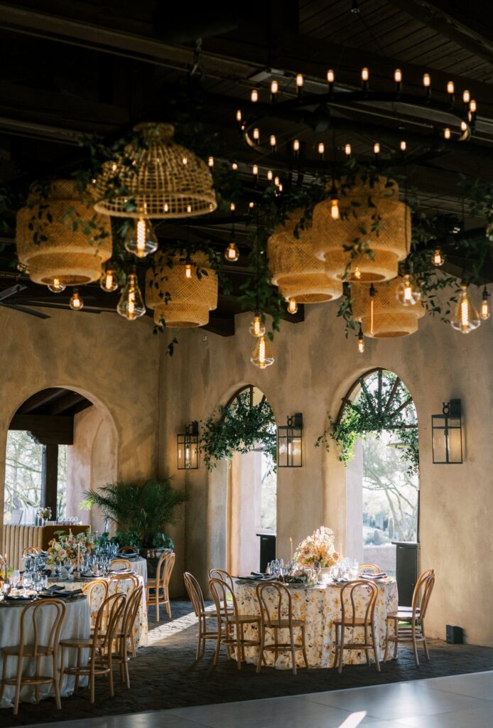 Windgate Ranch wedding reception with round tables, wicker light shades handing from ceiling with smilax.