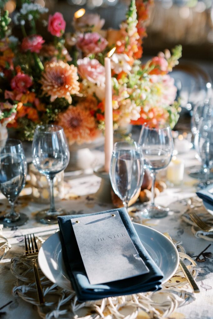 Wedding reception place setting and centerpiece of white, pink, gold, peach, and mauve flowers.