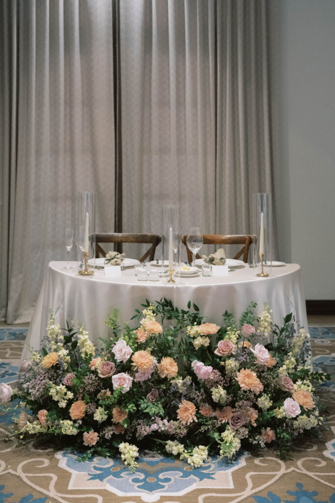 Wedding reception sweetheart table with taper candles and ground floral arrangment in front.