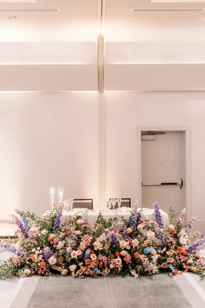 Indoor wedding reception sweetheart table large ground floral in front of table.