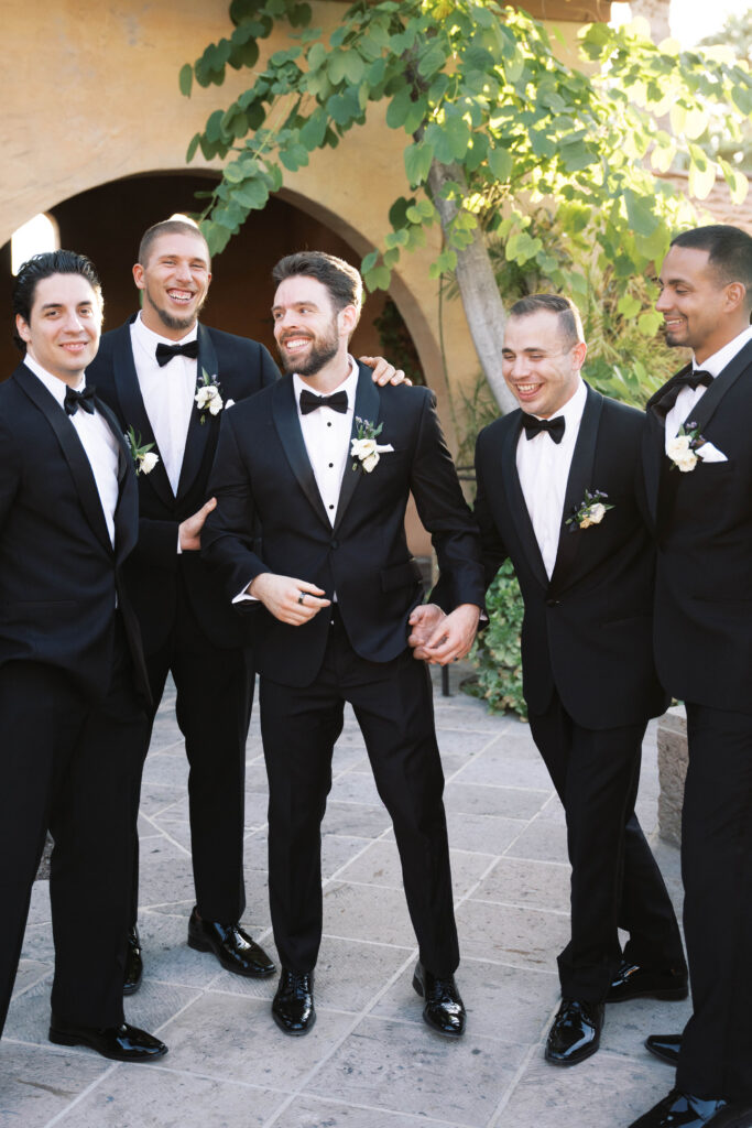 Groom with groomsmen in black suits with bow ties and boutonnieres.