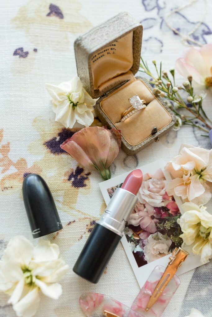 Detailed flat lay of wedding bridal ring, polaroid picture of flowers, pink lipstick, hair pins.