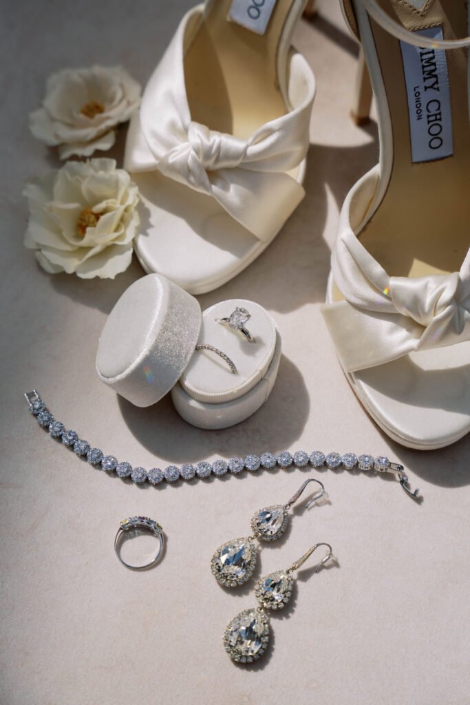 Bridal details of white bridal shoes, rings, bracelet, ring, and earrings.