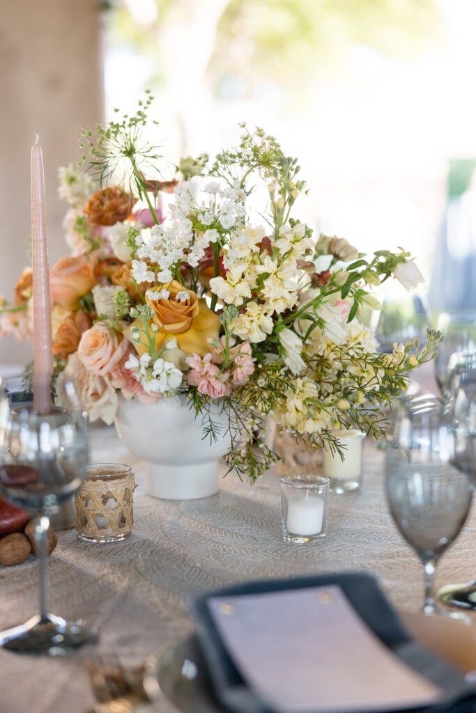 Wedding reception centerpiece of white, yellow, and pink flowers in white vase.