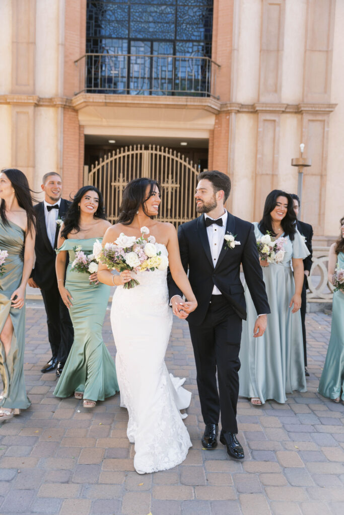 Bride and groom walking, holding hands, with bridal party walking behind them.