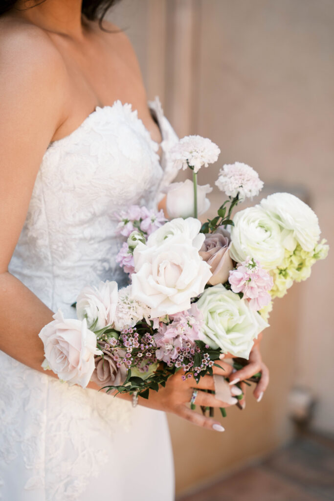 Bride holding bouquet of white, purple, cream, and pink flowers including roses.