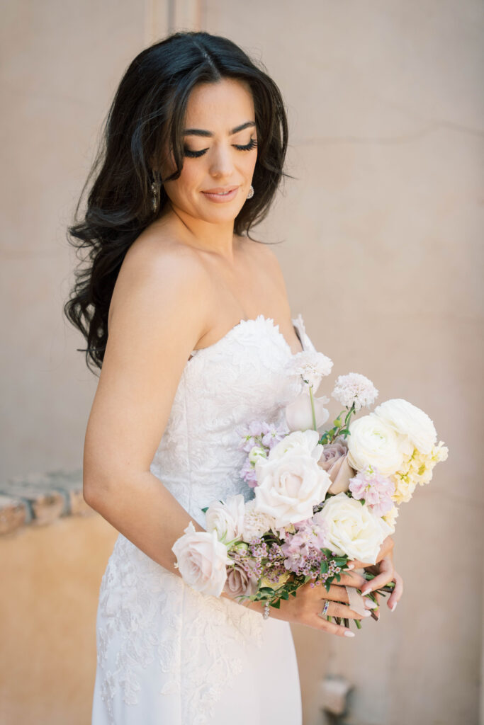 Bride holding bouquet of white and light purple flowers, looking down on it.