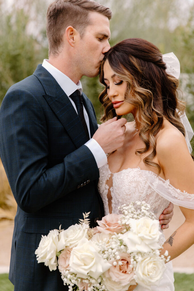 Groom kissing the top of bride's head, both with eyes closed.