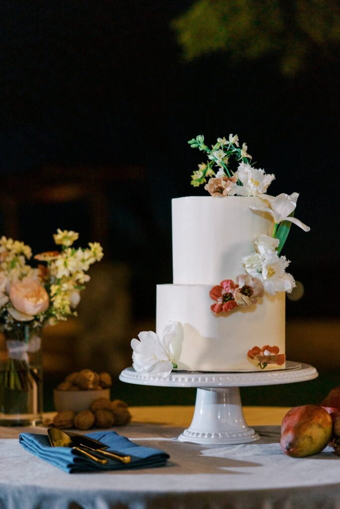 Two tiered white wedding cake with flowers added.