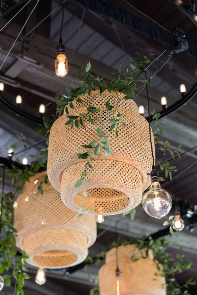 Wicker lamp shades hanging from ceiling some greenery draping around them.