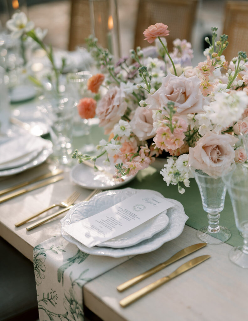 Lush floral reception centerpiece in pink, peach, and white floral shades on sage green runner down center.