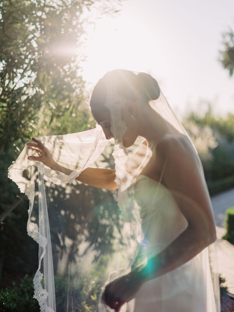 Bride holding sheer veil out to side with one hand, looking down.