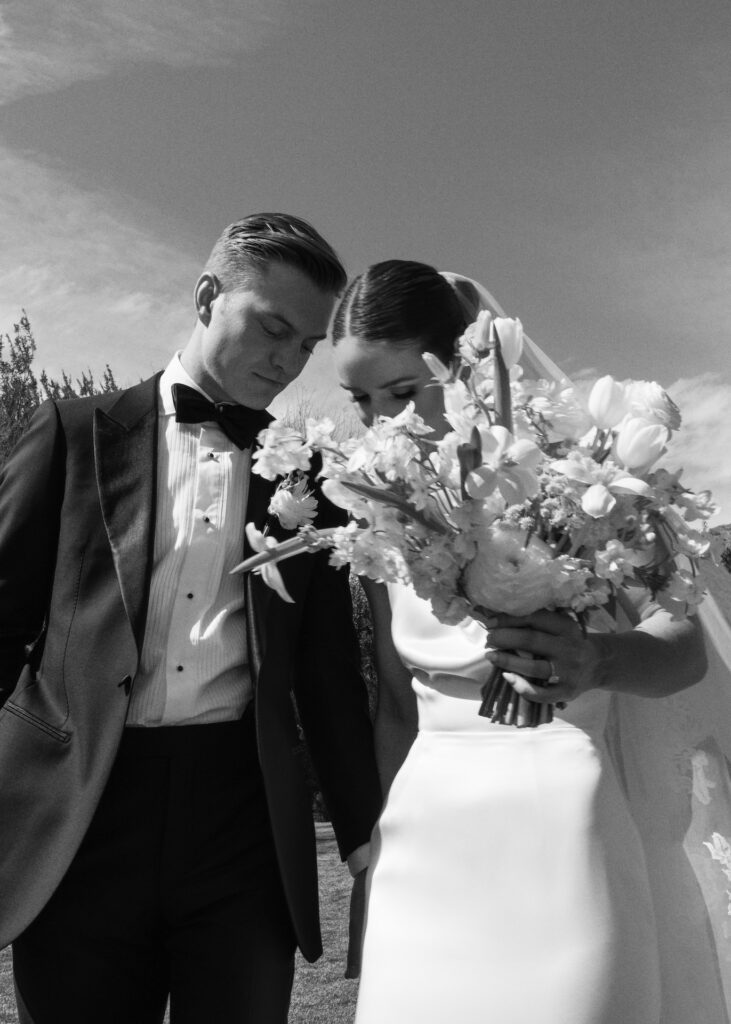 Bride and groom holding hands, looking down, bride holding bouquets.