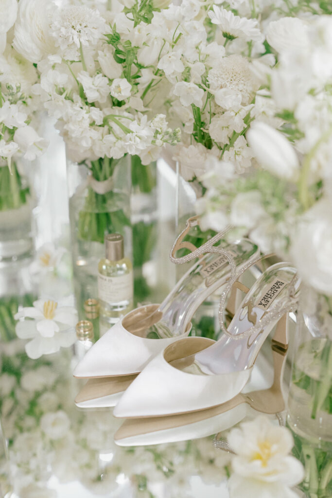 Bridal details of shoes, perfume, rings, and bouquet in glass vase.