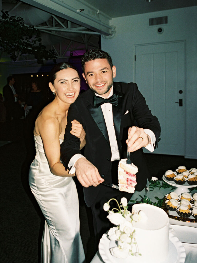 Bride and groom cutting wedding cake with pink filling, smiling, embracing.