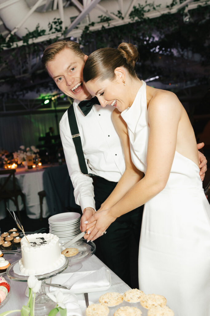 Bride and groom cutting small white wedding cake together.