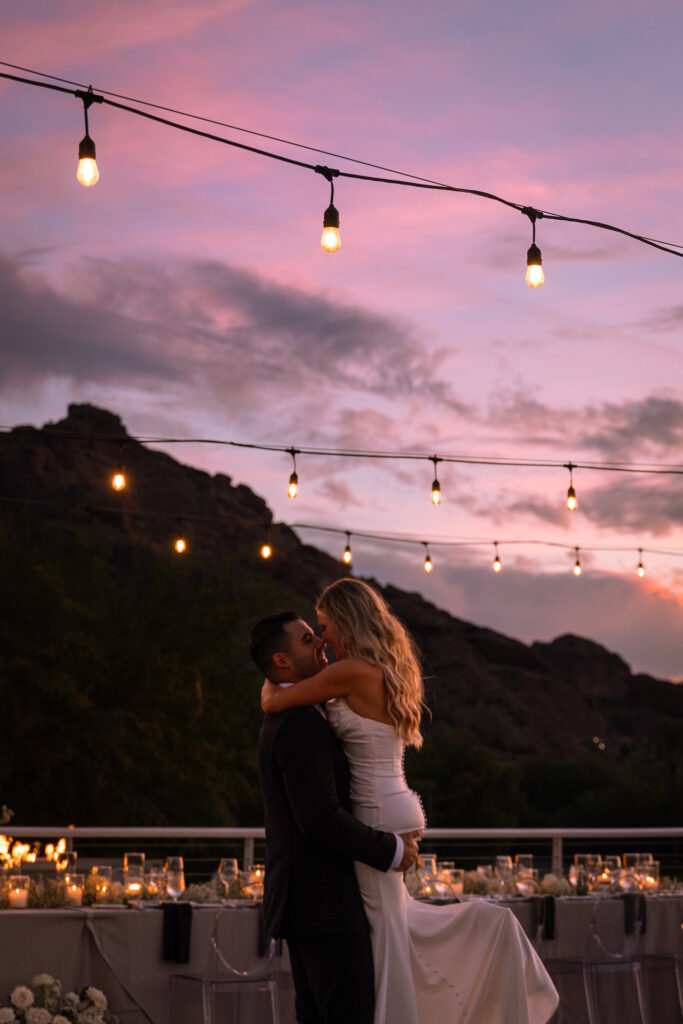 Groom lifting up bride, their noses touching on Mountain Shadows patio with Camelback Mountain in the background.