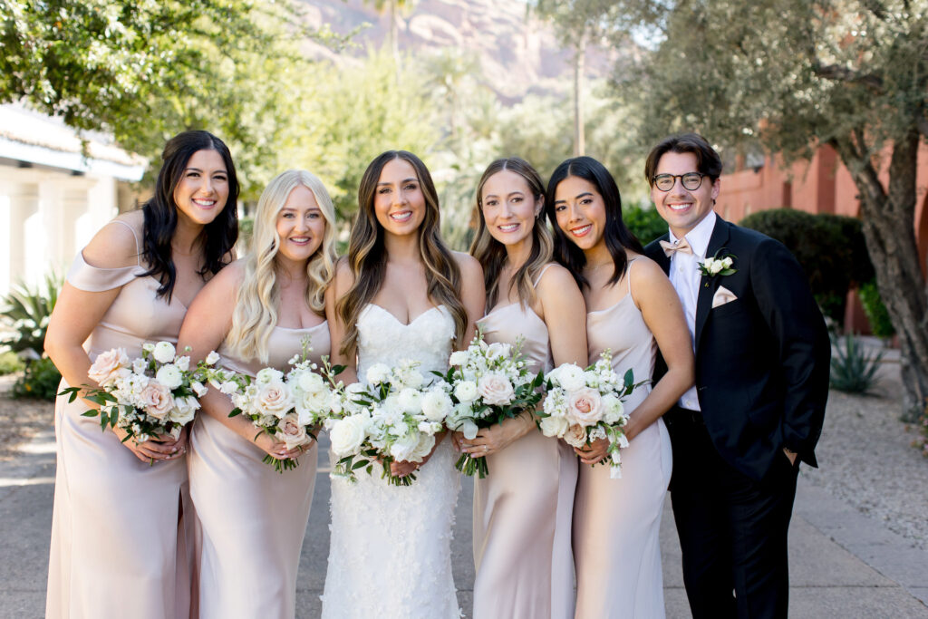 Bride standing in row with bridesmaids wearing blush dresses and a brides-man in black suit.