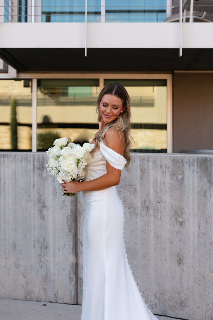 Bride looking over shoulder and down holding bouquet of white roses.