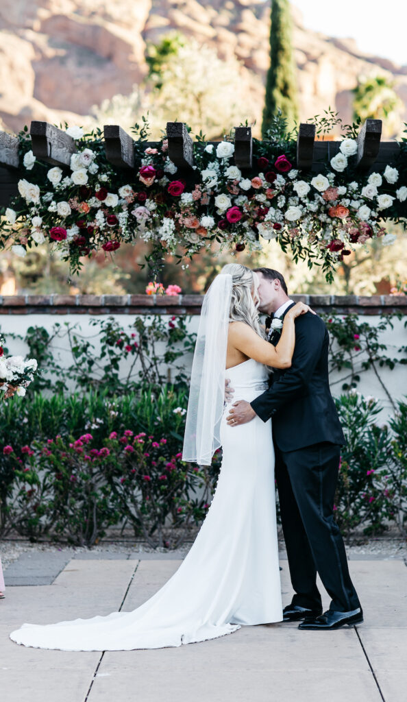 Bride and groom kissing under Omni Montelucia pergola with flowers added to it.