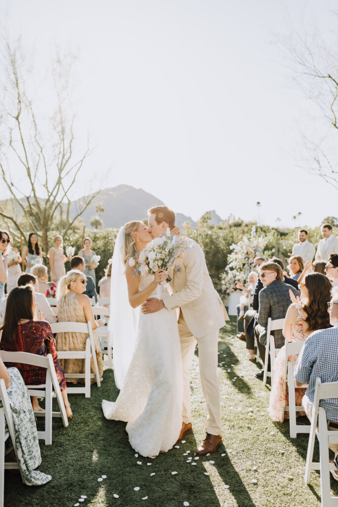 Bride and groom kissing in wedding ceremony aisle.