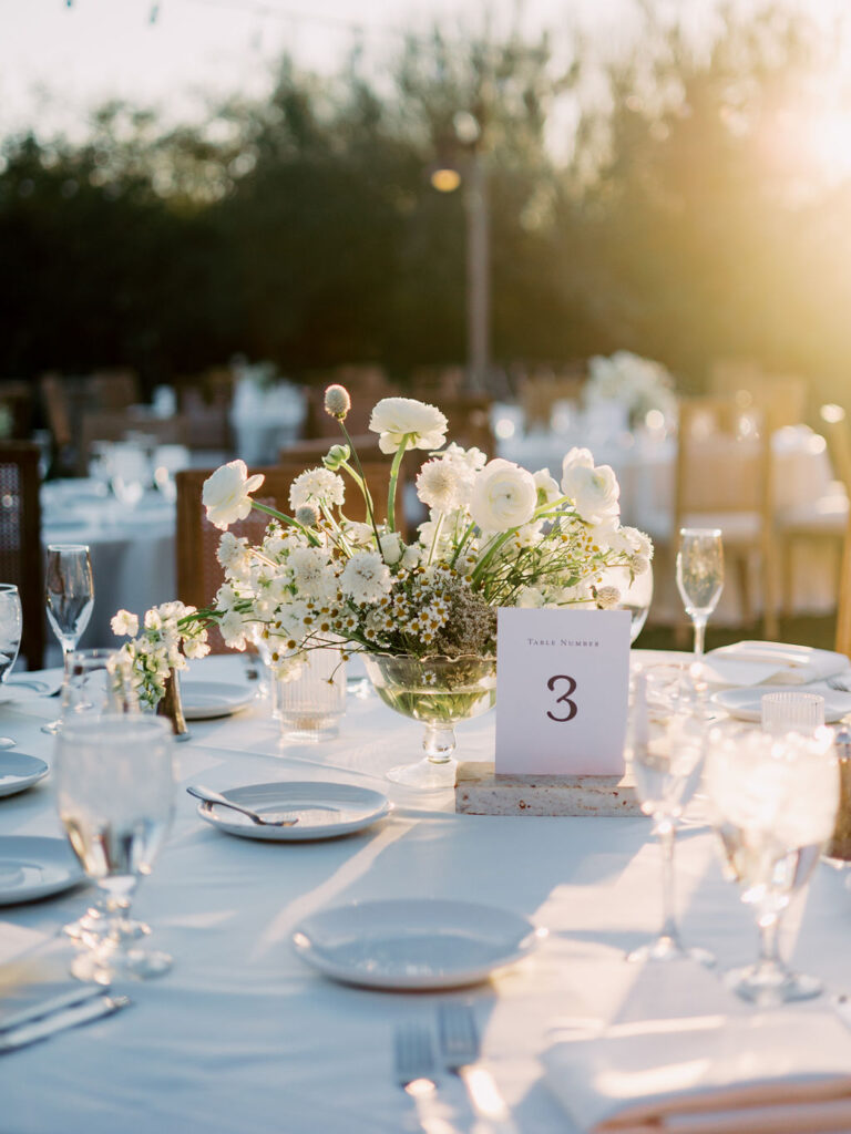 Outdoor wedding reception with centerpiece of white flowers in a glass vase.