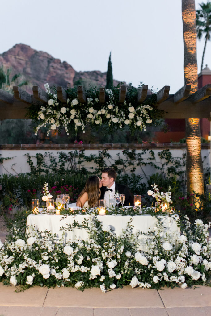 Bride and groom kissing while sitting at head table.