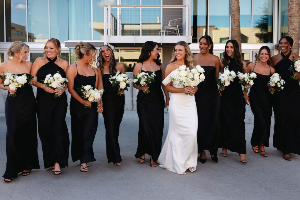 Bride walking in a line with bridesmaids in various styles black dresses.