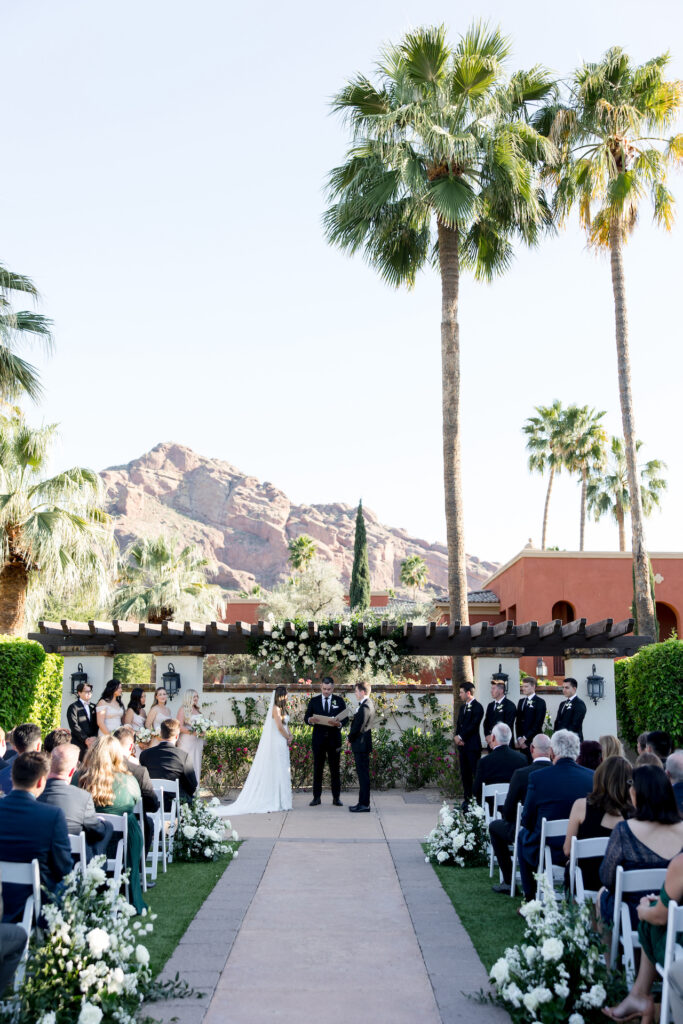 Bride and groom standing in wedding ceremony altar space with guests looking on and wedding party standing to their sides.