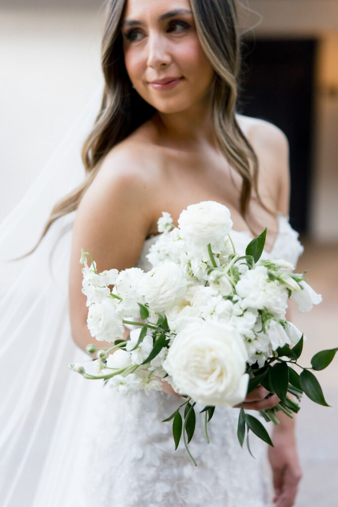 Bride looking over her shoulder holding bouquet of white flowers and greenery.