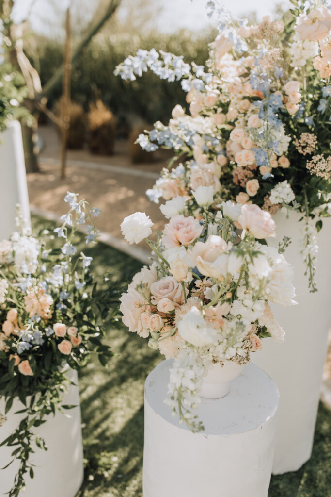 Ceremony altar space wedding flowers placed on round cylinder pillars of white, blush, and blue flowers with greenery.