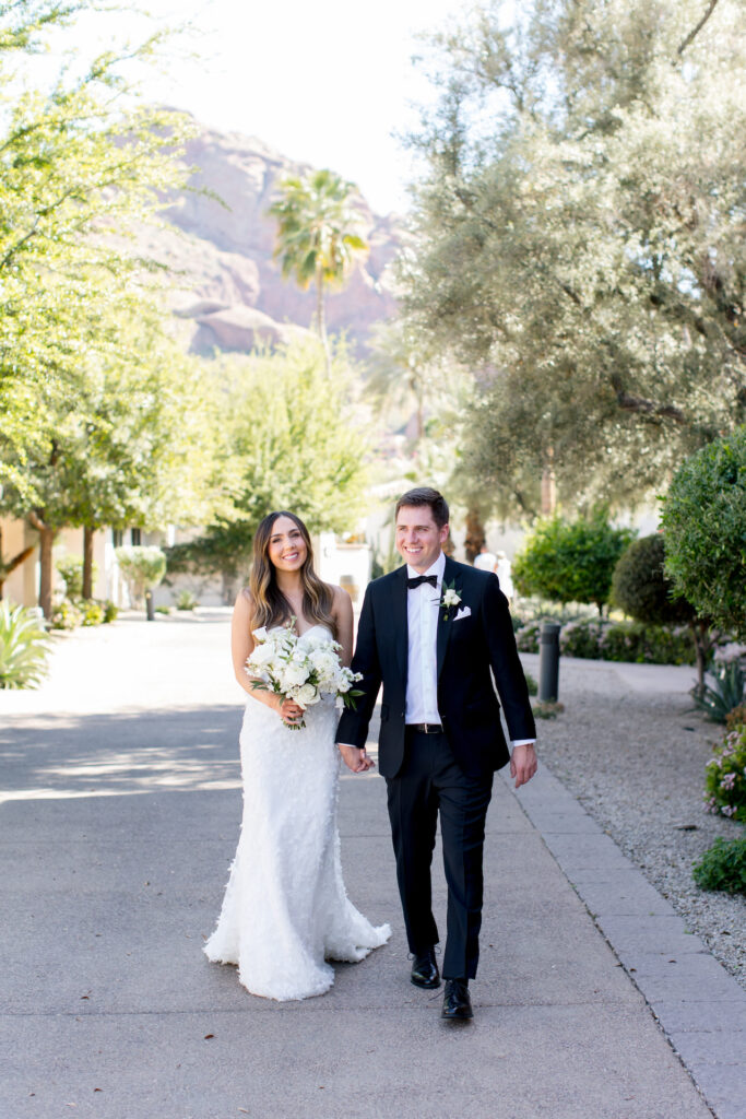 Bride and groom walking and holding hands at Omni Montelucia, bride holding bouquet.