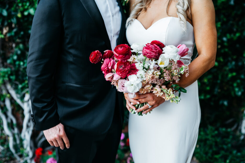 Groom standing next to bride who is holding a bridal bouquet of white and shades of pink flowers.