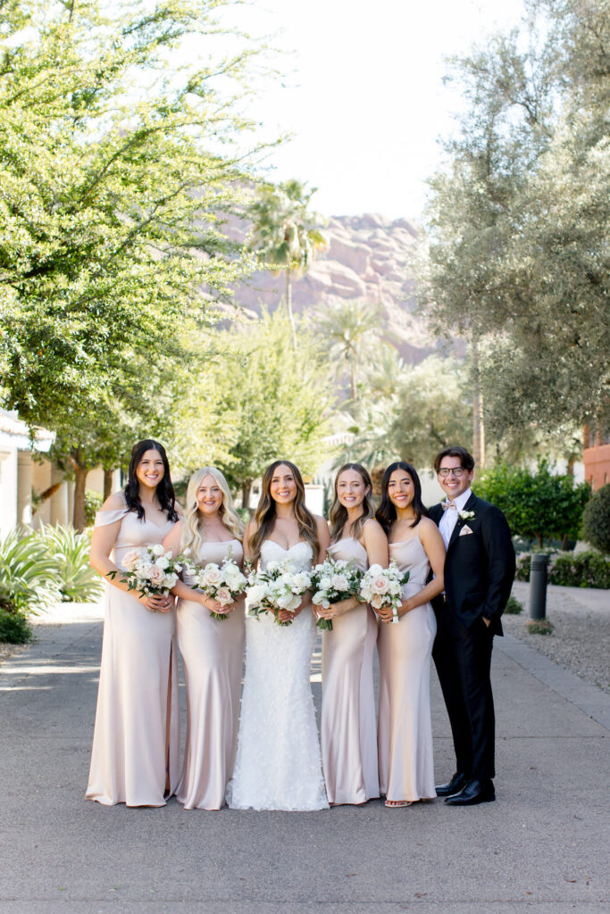 Bride standing in row with bridesmaids wearing blush dresses and a brides-man in black suit.