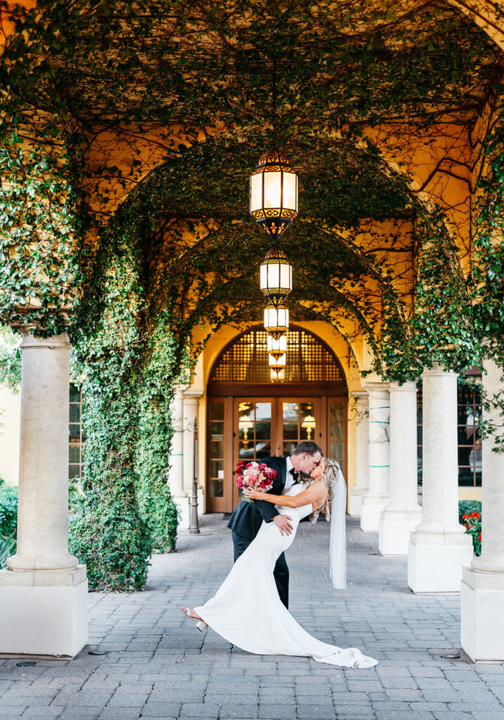 Groom dipping bride and kissing her under archway with elegant lanterns hanging from ceiling at Omni Montelucia resort.