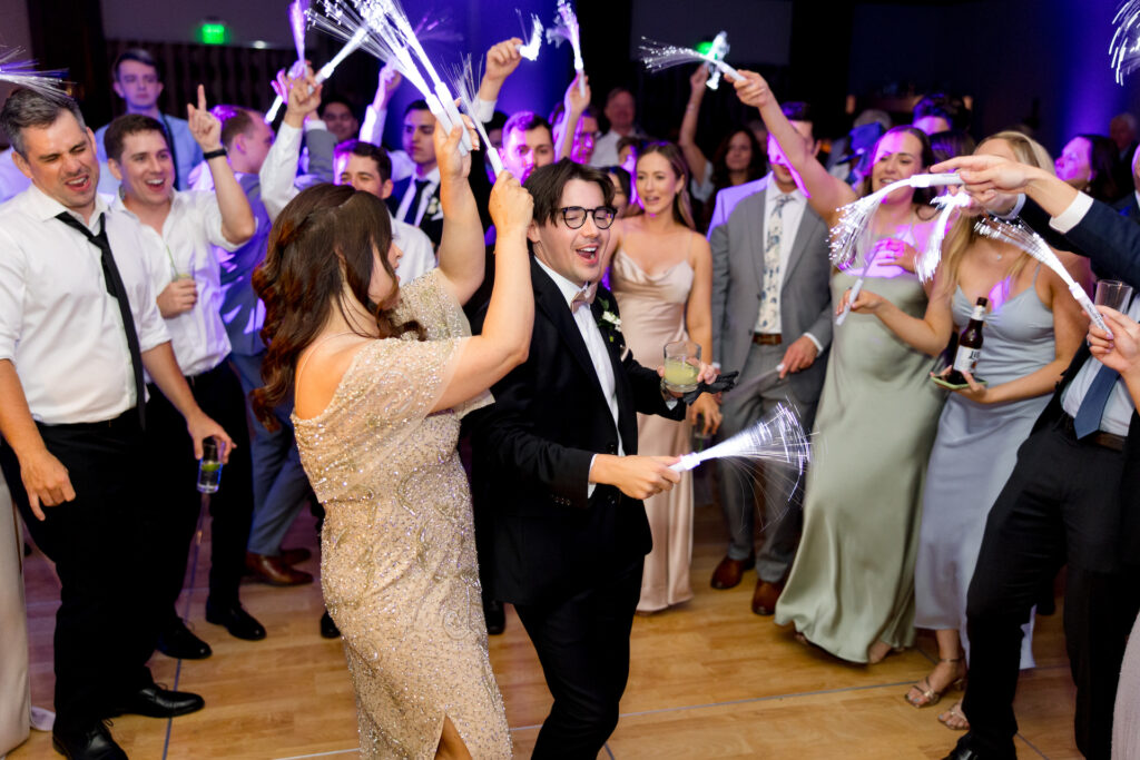 Wedding guests dancing at reception and waving electric sparklers.