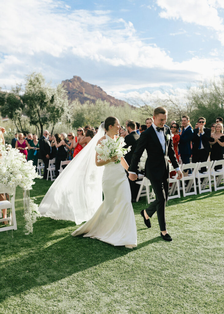 Bride and groom exiting outdoor wedding ceremony aisle holding hands.