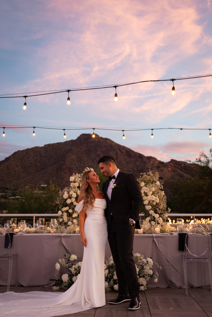 Bride and groom with arms around each other standing in front of reception table with flower decor at Mountain Shadows, smiling at each other.