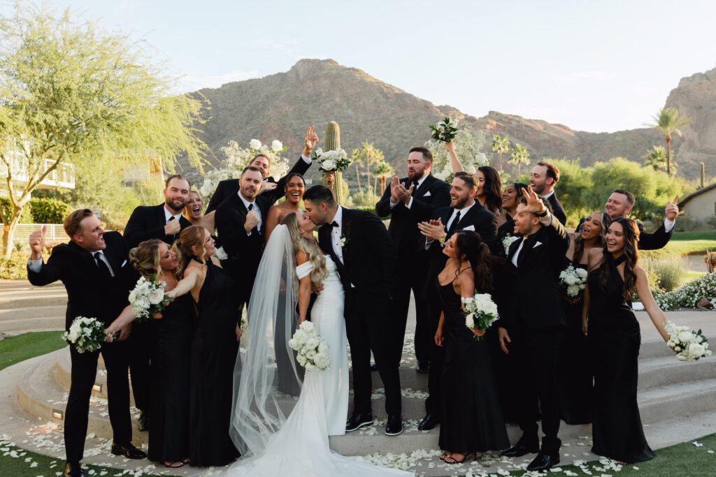 Bride and groom kissing in the center of their wedding party celebrating around them on the ceremony altar steps.