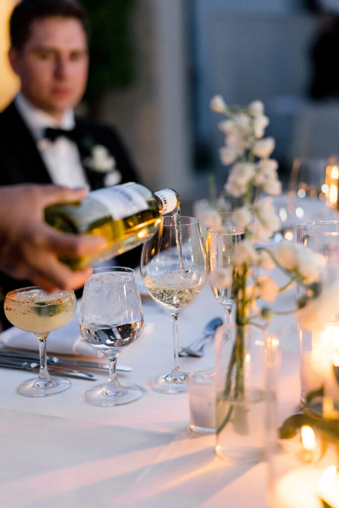 Wine being poured into glass with groom sitting looking on in background.